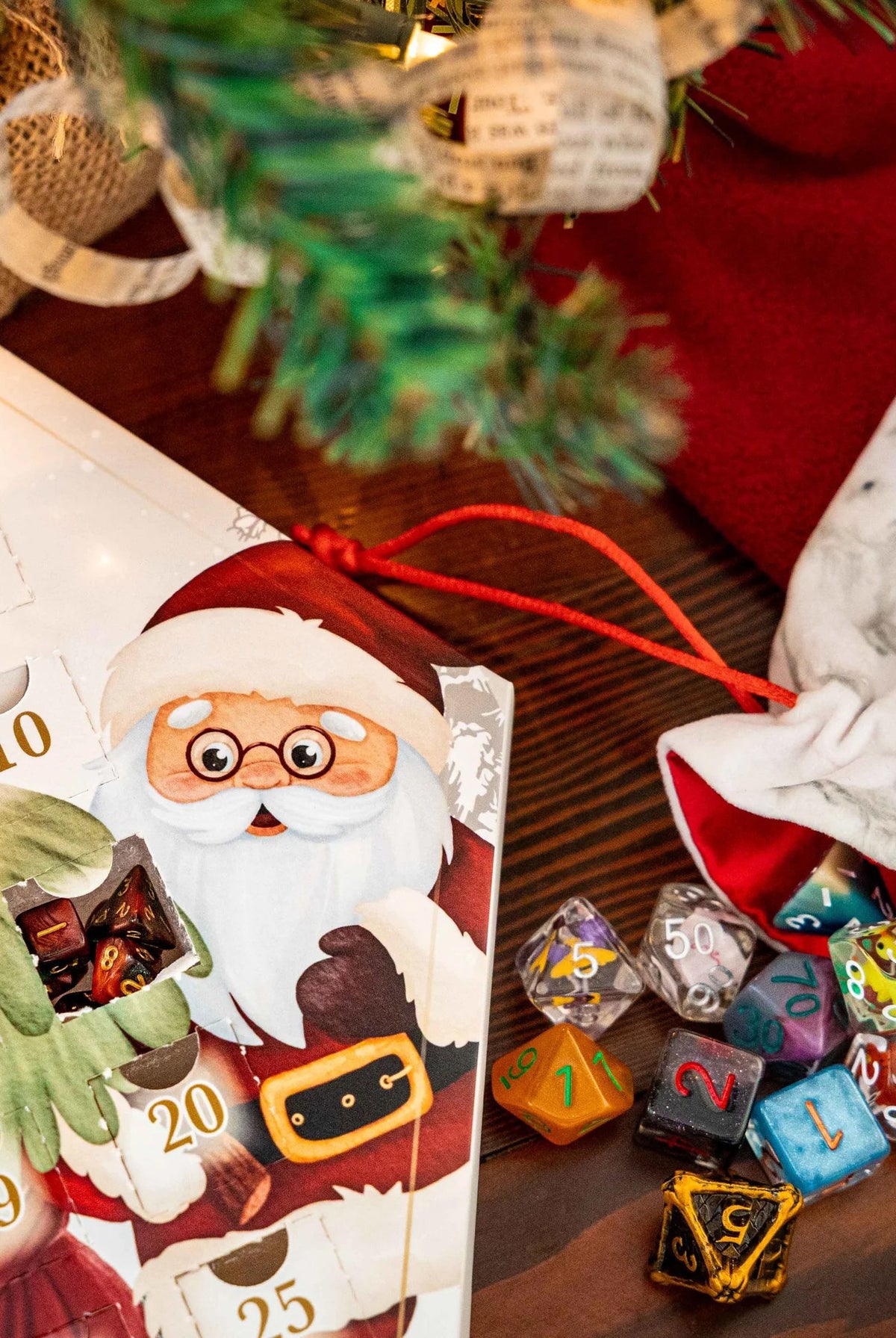 FanRoll Christmas Dice Advent Calendar displayed beside colorful polyhedral dice and a holiday dice bag under a Christmas tree