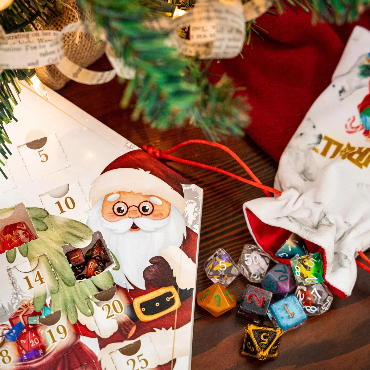 FanRoll Christmas Dice Advent Calendar displayed beside colorful polyhedral dice and a holiday dice bag under a Christmas tree